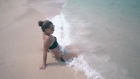 waves-wash-woman-body-lying-on-beach-in-black-swimsuit