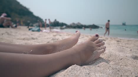 lady-feet-lie-on-sand-beach-against-turquoise-clean-ocean