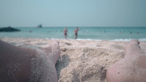 fellow-feet-in-beach-sand-against-blue-ocean-waves-in-summer