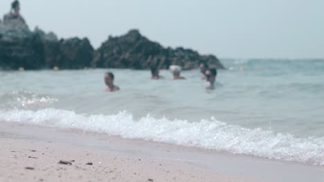 white-foaming-waves-roll-on-sand-beach-against-blurry-people