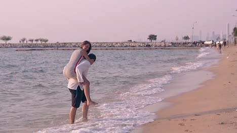 guy-carries-girl-on-back-out-of-waves-on-beach-slow-motion