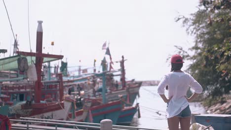 girl-in-long-white-shirt-and-red-cap-looks-at-moored-boats