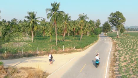 lady-rides-motorbike-along-road-against-palm-trees-aerial