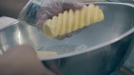 man-in-disposable-gloves-washes-pineapple-in-big-silver-bowl
