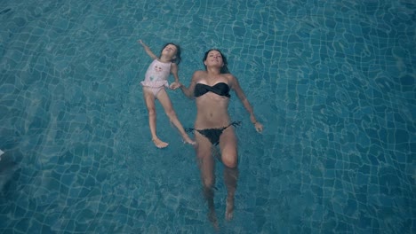 lady-in-black-bikini-and-little-girl-swim-on-back-in-pool