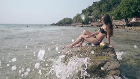 pretty-girl-with-cocktail-rests-on-rock-in-ocean-slow-motion