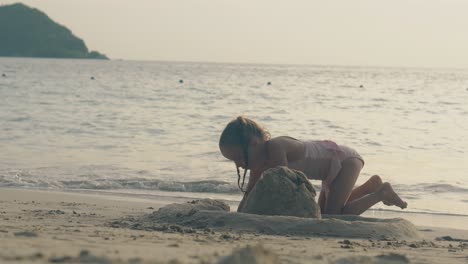 pretty-girl-in-pink-swimsuit-builds-sand-castle-on-sea-shore
