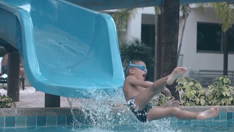 tanned-boy-slides-down-with-water-flow-into-pool-slow-motion