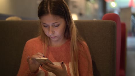 Young-beautiful-girl-sits-in-a-cafe-works-on-a-smartphone