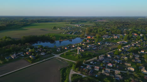 Aerial---Sideway-drone-view-of-serene-town-with-green-field-and-lake