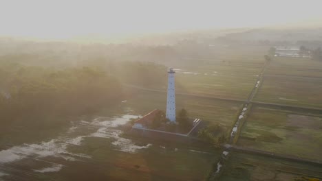 Foggy-morning-landscape-and-white-coastal-lighthouse,-aerial-orbit-view