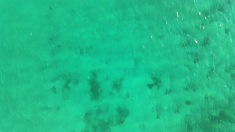 Top-down-view-patterns-on-crystal-clear-turquoise-tropical-ocean-water-by-a-sandy-shore