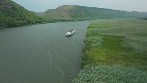 rapid-removal-from-the-ship-that-moves-along-the-river,-a-side-wind-is-visible-that-raises-waves-and-ripples-on-the-water,-the-reeds-sway