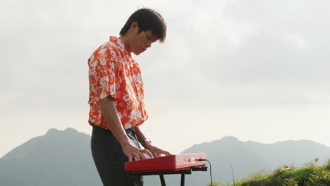 Asian-playing-keyboard-at-mountain-in-Vietnam,-side-view-slow-motion