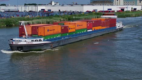 Großes-Schiff,-Das-Schiffscontainer-Auf-Dem-Seeweg-Transportiert,-Mit-Industriegebäuden-Im-Hintergrund