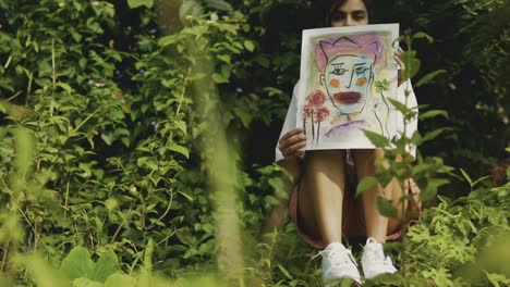 A-pretty-girl-sitting-between-plants-expressing-her-emotions-by-showing-an-abstract-drawing