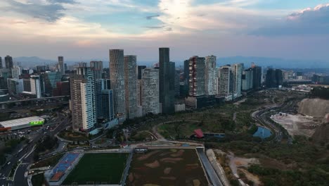 Line-of-skyscrapers-in-front-of-the-La-Mexicana-Park,-evening-in-Santa-Fe,-Mexico---Aerial-view