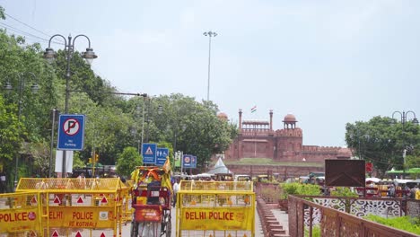 Toma-Panorámica-Del-Fuerte-Rojo-En-Nueva-Delhi,-India,-Con-Auto-Rikshaws-Y-Barricada-Policial-En-Primer-Plano