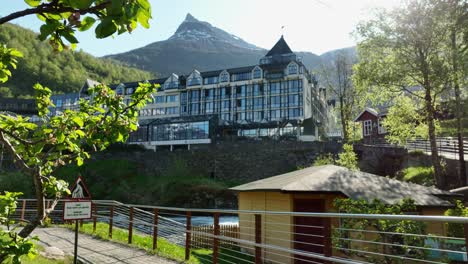 Unweiling-luxury-hotel-Union-in-Geiranger-Norway-from-behind-a-closeup-apple-tree-branch---Pointy-mountain-peak-in-background