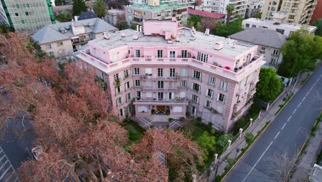 Luftaufnahme-über-Dem-Rosa-Wohngebäude-In-Providencia,-Santiago,-Chile.-Ein-Paar-Geht-Mit-Herbstbäumen-Auf-Den-Eingang-Zu