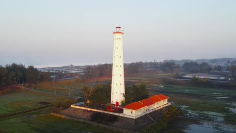 Scenic-lighthouse-with-bright-orange-roofs-in-morning-sunrise,-aerial-orbit
