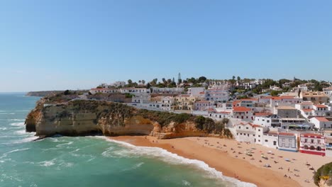 Carvoeiro-coastal-villas-and-tourists-sunbathing-on-beach,-Aerial-reverse-dolly