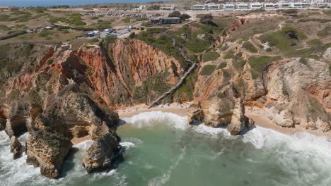 wooden-stairs-leading-down-to-sandy-beach-of-ponta-da-piedade,-Drone-pulls-back-rising