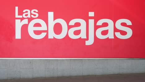 Los-Compradores-Pasan-Junto-A-Un-Gran-Cartel-Que-Anuncia-La-Temporada-De-Rebajas-De-Verano-Fuera-De-Los-Grandes-Almacenes-Más-Grandes-De-España,-El-Corte-Inglés,-En-España.