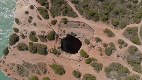 Drone-Elevándose-Sobre-La-Cueva-De-Benagil,-Vista-Aérea-De-Arriba-Hacia-Abajo,-Senderos-Arenosos-Alrededor
