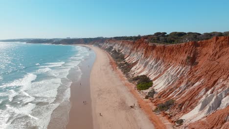 tourists-and-locals-walking-along-beautiful-golden-sand-on-praia-da-falesia,-Aerial-trucking-pan