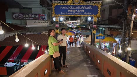 Taking-a-selfie-in-front-of-the-Amphawa-Floating-Market's-arch,-right-across-the-bridge-to-the-night-market-in-Amphawa,-Samut-Songkhram,-Thailand