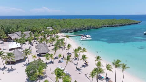 Aerial-flyover-tropical-beach-with-palm-trees-and-parking-boats-on-Tropical-Island-on-Dominican-Republic---Establishing-drone-shot