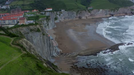 Epic-cliffside-beach-of-Itzurun,-aerial-rising-dolly-above-strong-crashing-waves