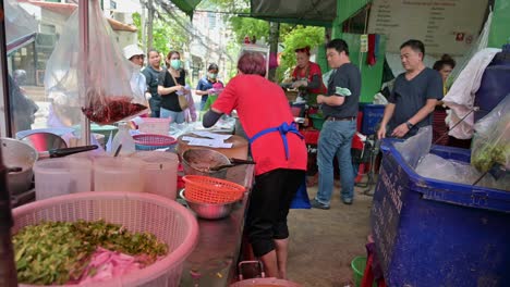 A-famous-local-hawker-getting-orders-of-grilled-chicken-and-pork-in-the-street-of-Bangkok,-Thailand