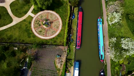 Top-view-rising-tilt-up-reveals-grand-union-canal-barge-boats-along-river-in-Stoke-Bruerne