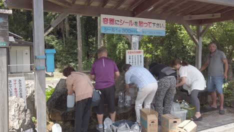 Japaner-Füllen-Flaschen-Mit-Natürlichem-Mineralwasser-Aus-Dem-Tentokuji-Tempel-In-Den-Bergen,-Einer-Gesunden-Quelle