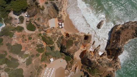 Top-view-of-Praia-dos-tres-Irmaos-beach-bungalow-umbrellas-and-crashing-waves
