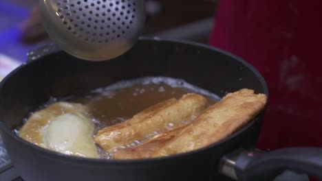 Meat-roll-and-samosa-deep-fried-and-stirred-in-oil-hot-oil,-filmed-as-close-up-in-handheld-style