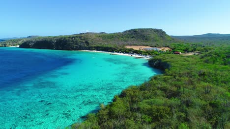 Drone-rises-above-curacao-shrubland-to-reveal-iconic-sandy-beach-and-deep-blue-turquoise-water