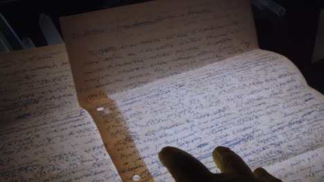Hands-of-a-forensic-specialist-wearing-protective-gloves-examine-handwritten-letters-on-a-backlit-table