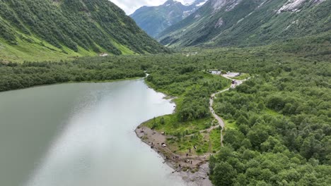 Glacial-lake-Brevatnet-and-lots-of-tourists-standing-on-beach-looking-at-Boyabreen-glacier-in-Fjaerland---Descending-aerial-with-tilt-up-to-reveal-lush-valley-in-background