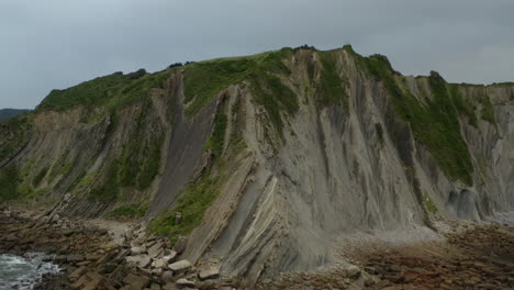 Sandy-rock-cliff-edge-pullback-aerial-to-reveal-large-shard-boulders-at-itzurun-beach-zumaia-spain