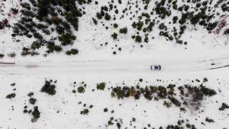 Vista-Aérea-De-Un-Coche-Blanco-Conduciendo-Por-Una-Carretera-Nevada-En-Invierno
