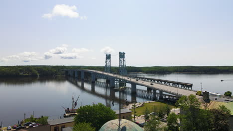 Descending-Drone-footage-showing-the-Sagadahoc-Bridge-and-the-Kennebec-River,-then-lowering-down-to-show-the-City-Hall-of-Bath