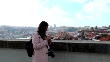 Woman-typing-on-her-phone-in-front-of-Porto-cityscape-on-cloudy-day