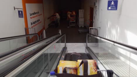 POV-person-with-shopping-bags-in-a-trolley-going-down-with-electric-escalator-after-shopping-in-the-Colruyt-supermarket---Brussels,-Belgium
