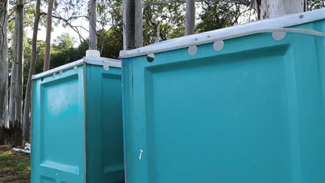 close-up-shot-of-aqua-green-blue-portable-bathrooms-in-eucalyptus-forest-setting-outdoors