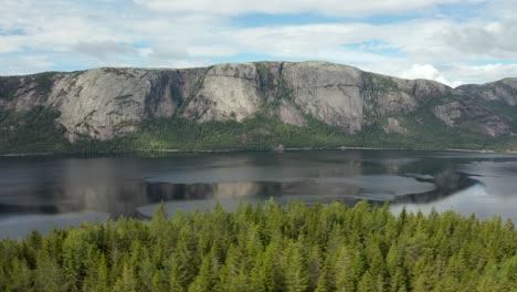 Aerial-past-a-forest-along-the-Nisser-lake-with-the-Langfjell-Mountain-range-in-the-background,-Treungen,-Telemark,-Norway