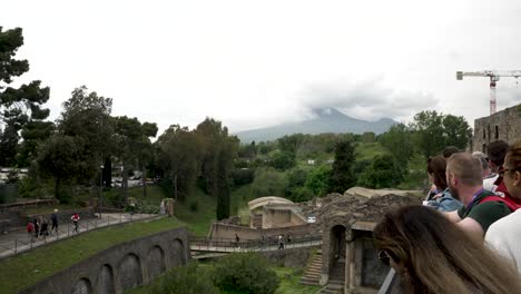 Tourists-Overlooking-Partial-Ruins-Of-Pompeii-With-Mount-Vesuvius-Covered-With-Clouds-In-Background