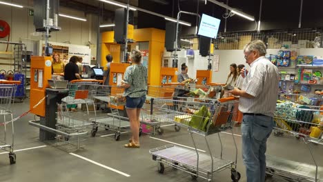 Customers-queueing-with-shopping-trolley-at-the-checkout-counter-of-the-Colruyt-warehouse-in-Brussels,-Belgium